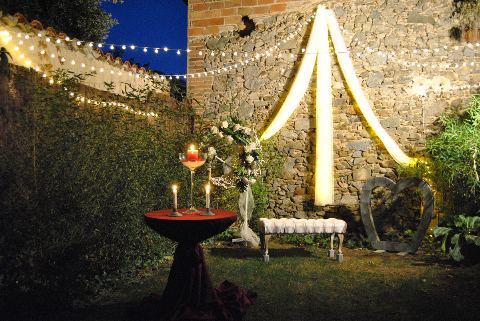 Altar de nit amb espelmes i flors, arc de teles il·luminat i garlanda de llums