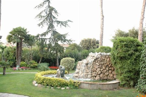 Font amb cascada de pedra i una escultura, envoltada de gespa i palmeres